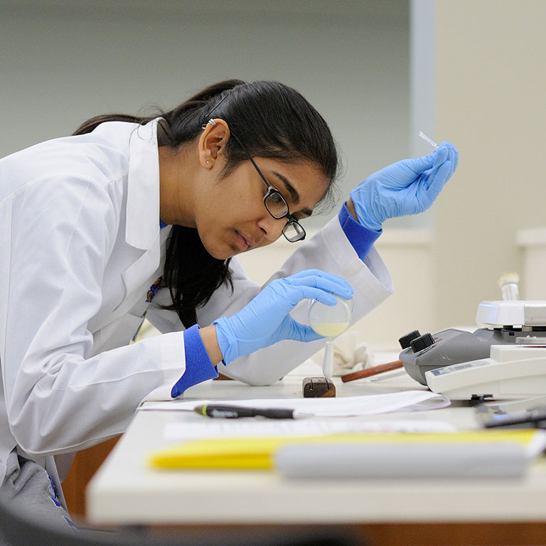 Researcher in lab coat and nitrile gloves works with sample in lab