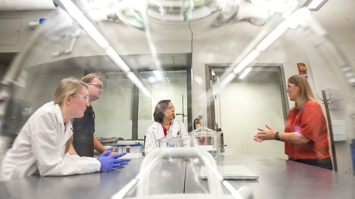 Four researchers has a conversation a lab - image shot through glass item in the lab